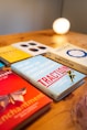 A collection of business and strategy books is displayed on a wooden surface. The books have titles related to customer growth and gamification. A warm light glows in the background, giving the scene a cozy, intellectual ambiance.