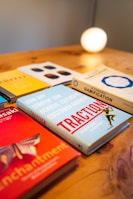 A collection of business and strategy books is displayed on a wooden surface. The books have titles related to customer growth and gamification. A warm light glows in the background, giving the scene a cozy, intellectual ambiance.