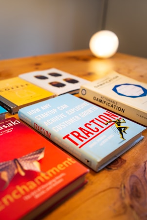 A collection of business and strategy books is displayed on a wooden surface. The books have titles related to customer growth and gamification. A warm light glows in the background, giving the scene a cozy, intellectual ambiance.