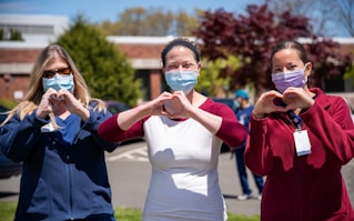 A lady wearing a PPE mask and  making the love emote at a charity event