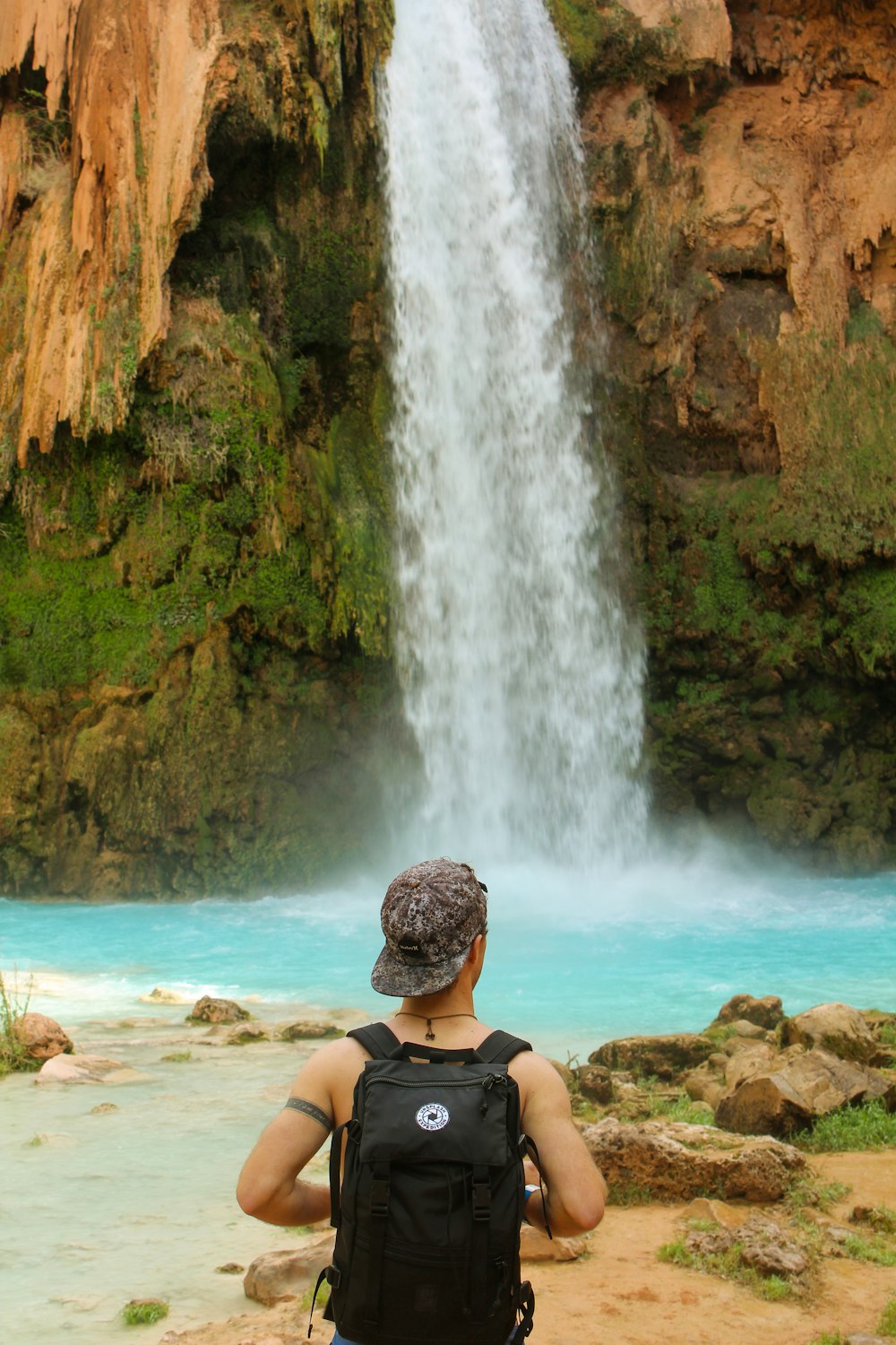 Frau im schwarzen Bikini sitzt tagsüber auf braunem Felsen in der Nähe von Wasserfällen