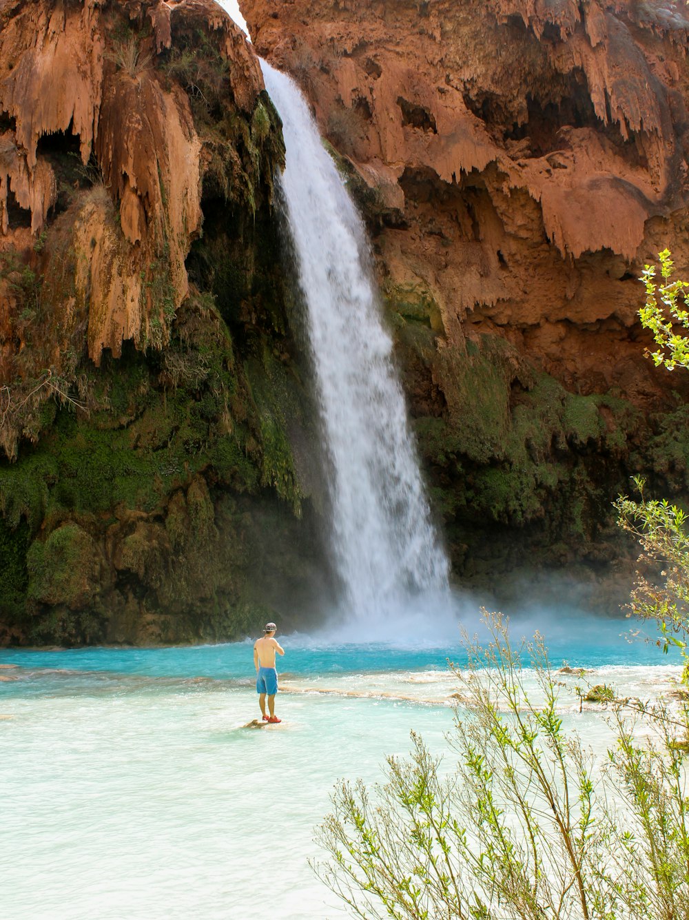 woman in red bikini standing on white sand near waterfalls during daytime