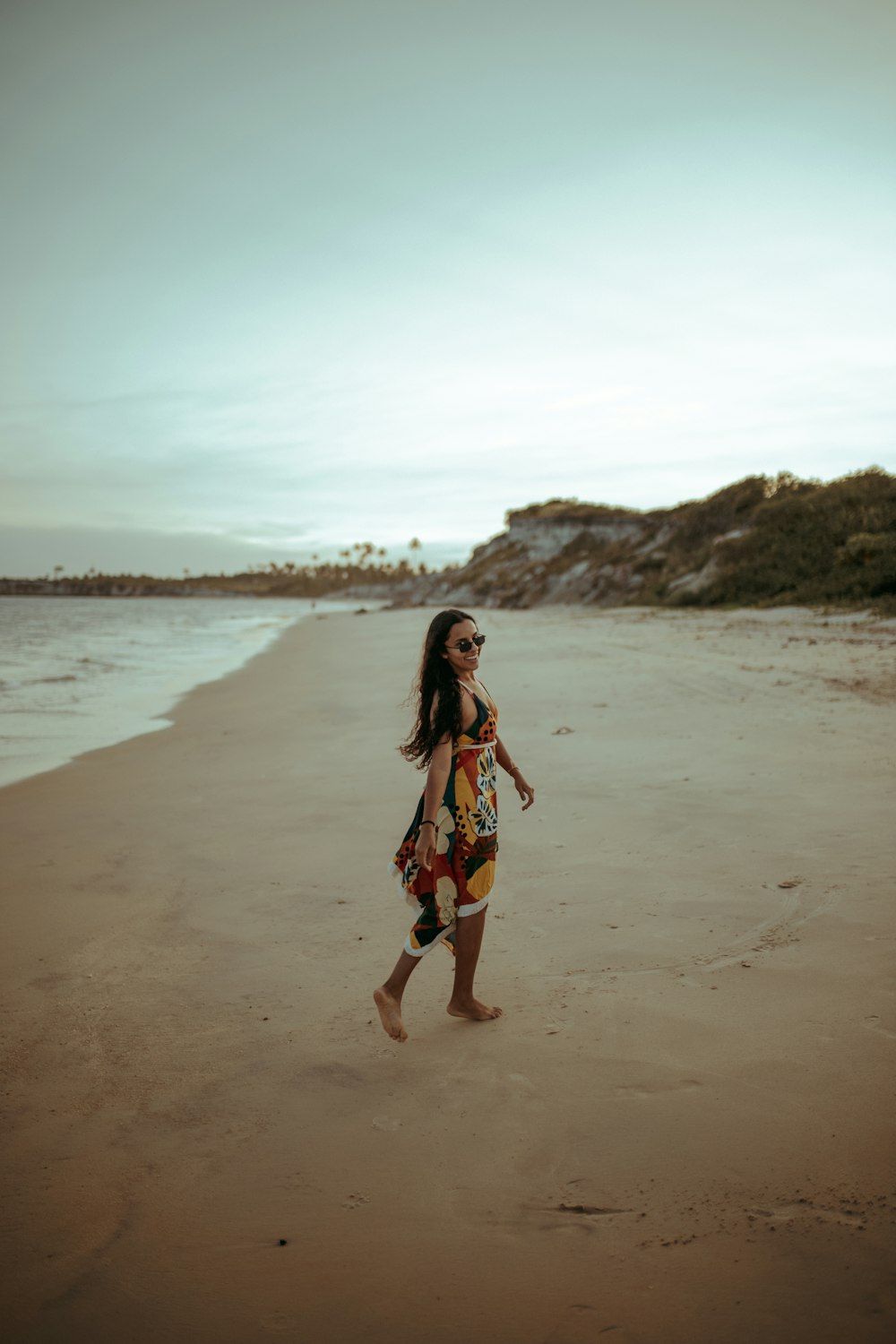 woman in blue and red floral dress walking on beach during daytime