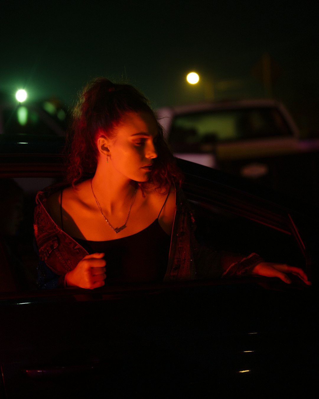 woman in brown spaghetti strap top standing in front of car during night time