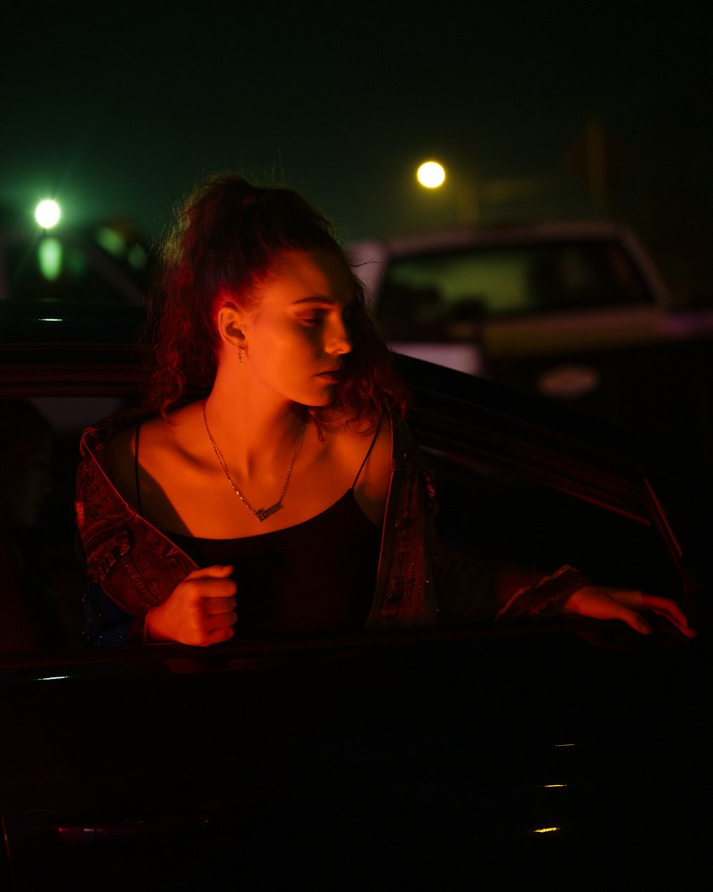갈색 스파게티 스트랩 탑을 입은 여자가 밤 시간에 차 앞에 서 있다