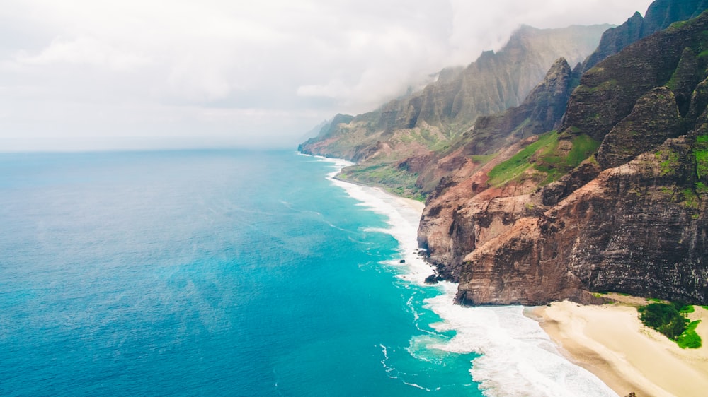 brown and green mountain beside blue sea during daytime