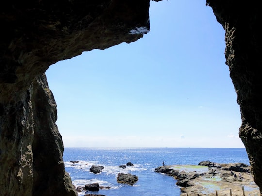 rocky shore with rocks under blue sky during daytime in Enoshima Iwaya Cave Japan