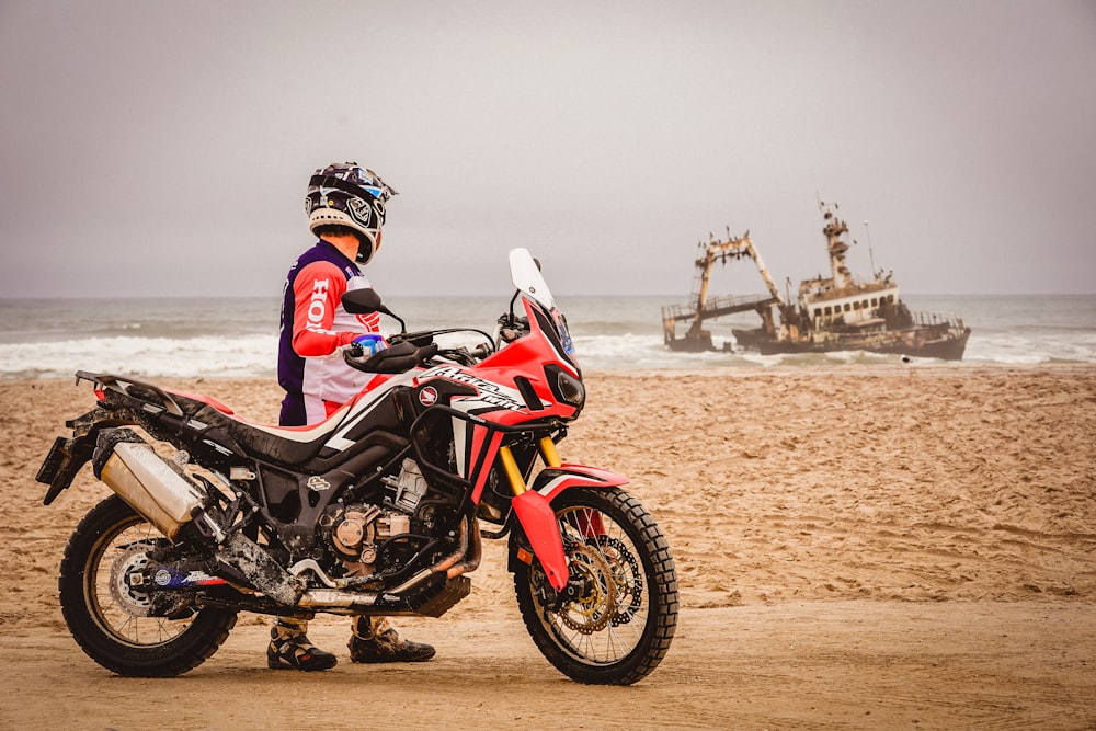 man in black and red motorcycle suit riding black and red sports bike on brown sand