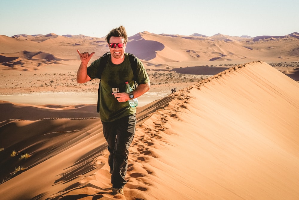 Mann in schwarzem Rundhals-T-Shirt und schwarzer Hose, der tagsüber auf braunem Sand steht