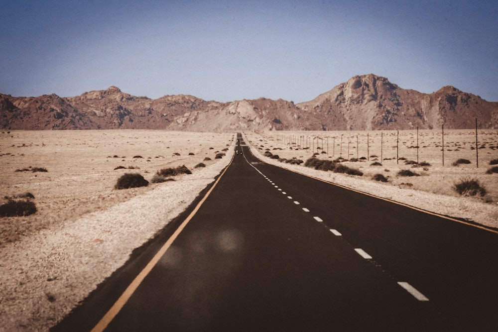 black asphalt road in between brown field under blue sky during daytime