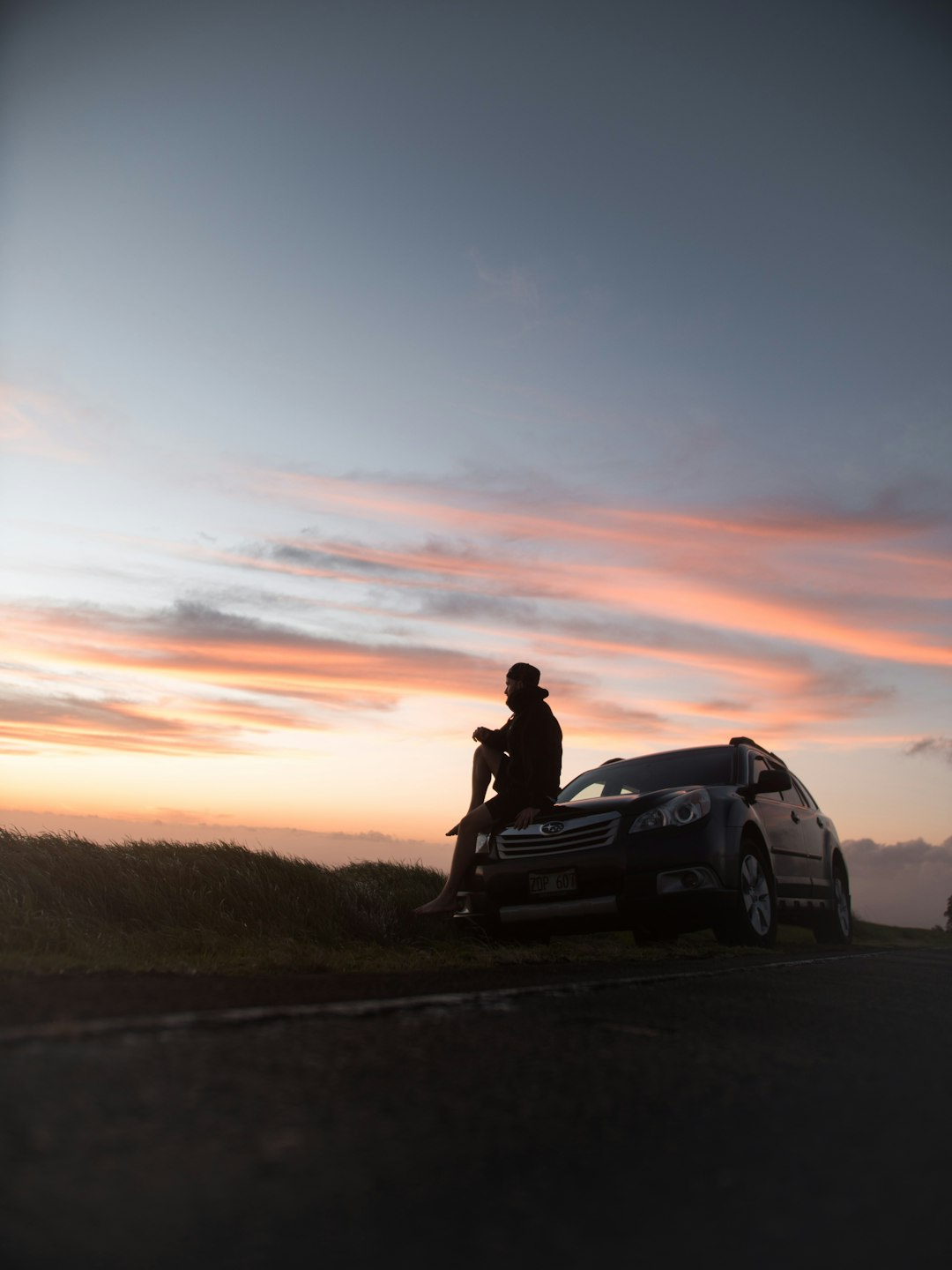 silhouette of man sitting on car hood during sunset