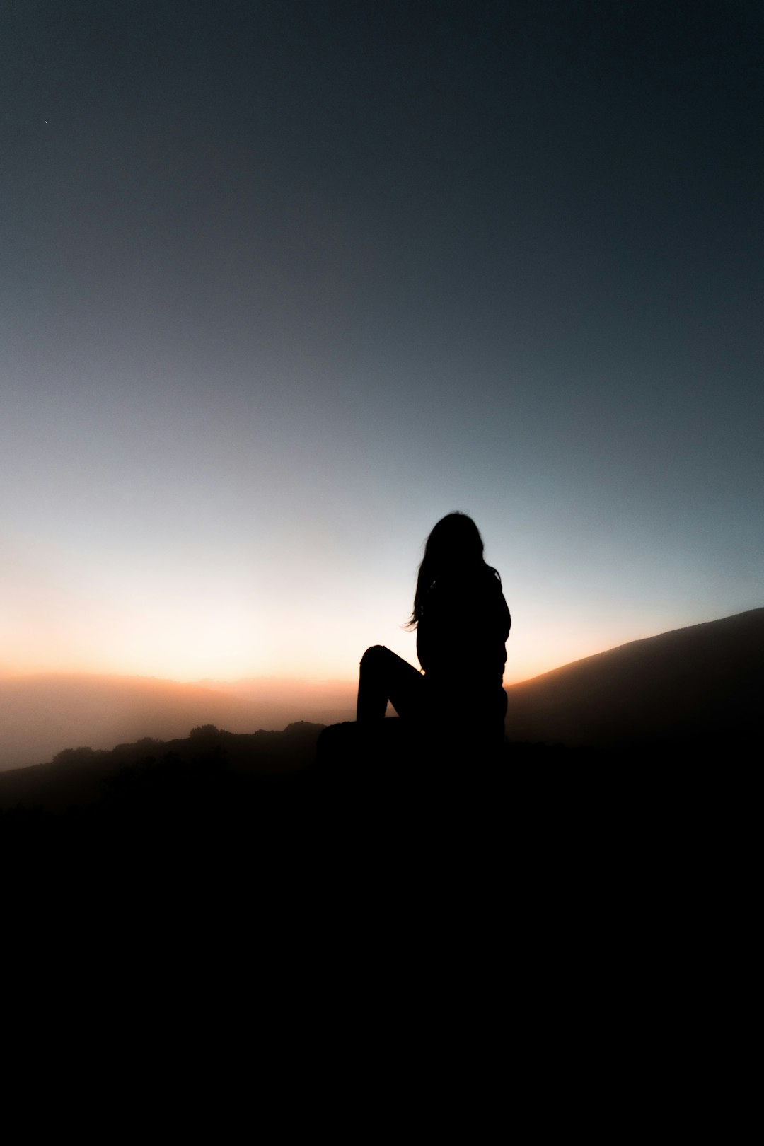 silhouette of woman sitting on rock during sunset