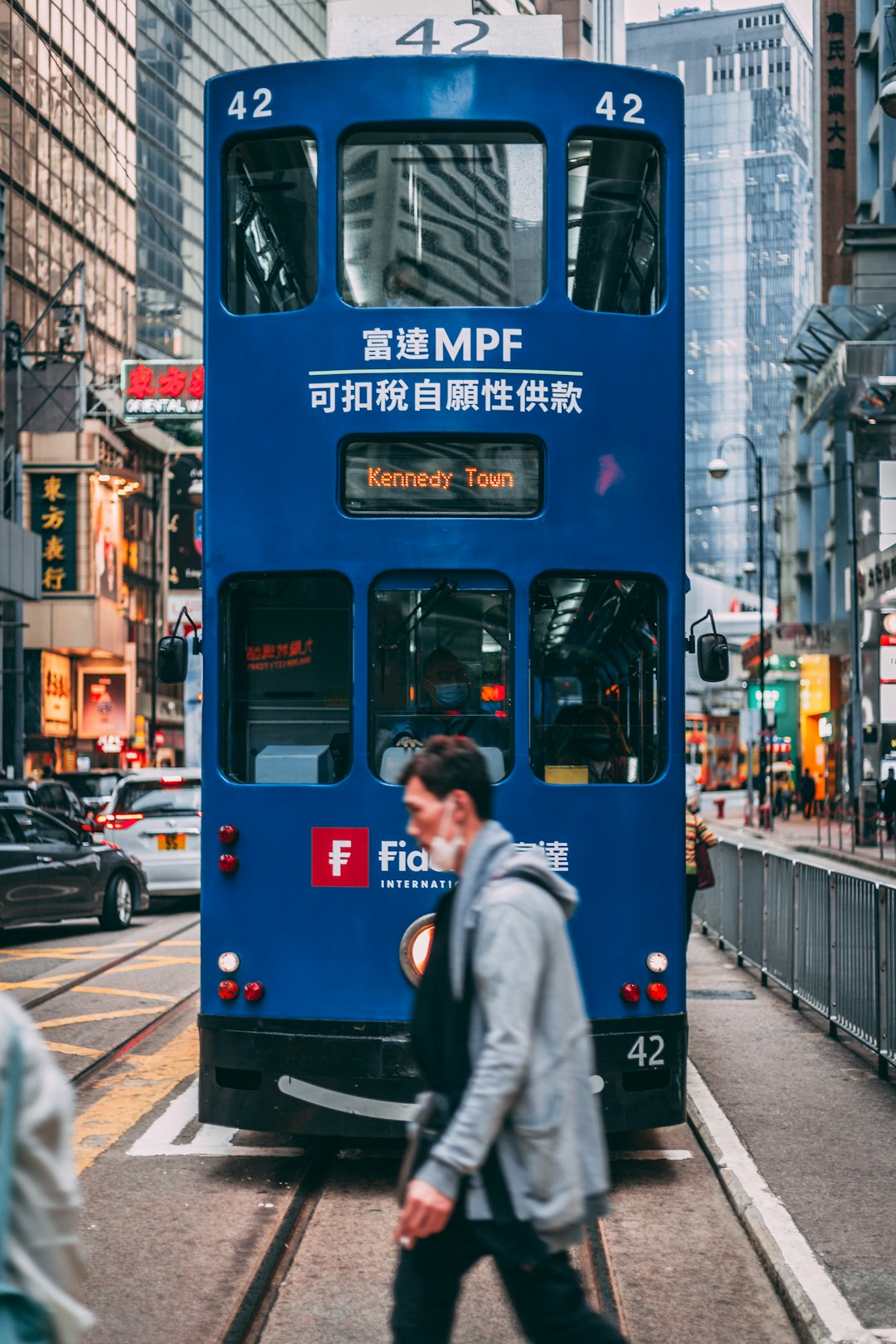 woman in gray coat standing beside blue and black tram during daytime