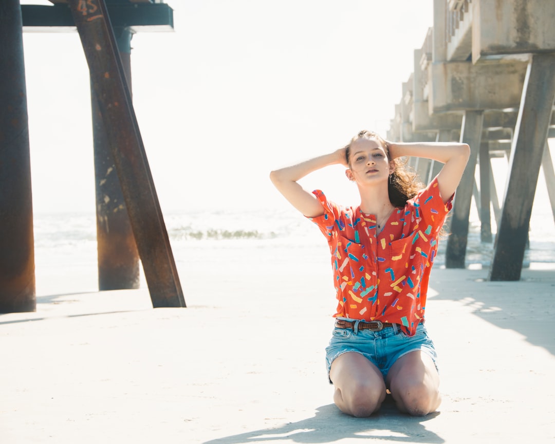 woman in orange and blue floral sleeveless dress sitting on white sand during daytime