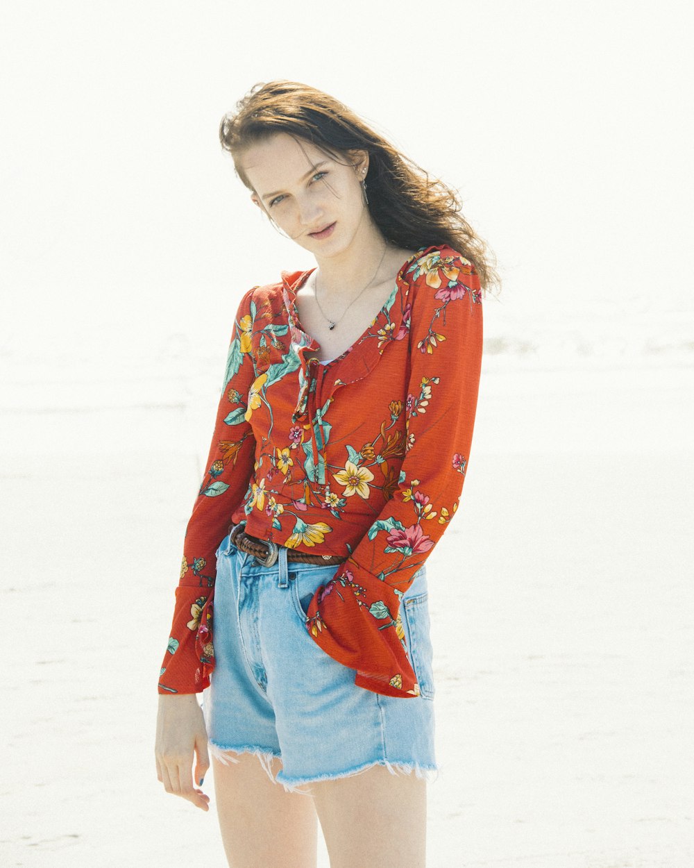 昼間、白い砂浜に立つ赤と青の花柄の長袖シャツを着た女性