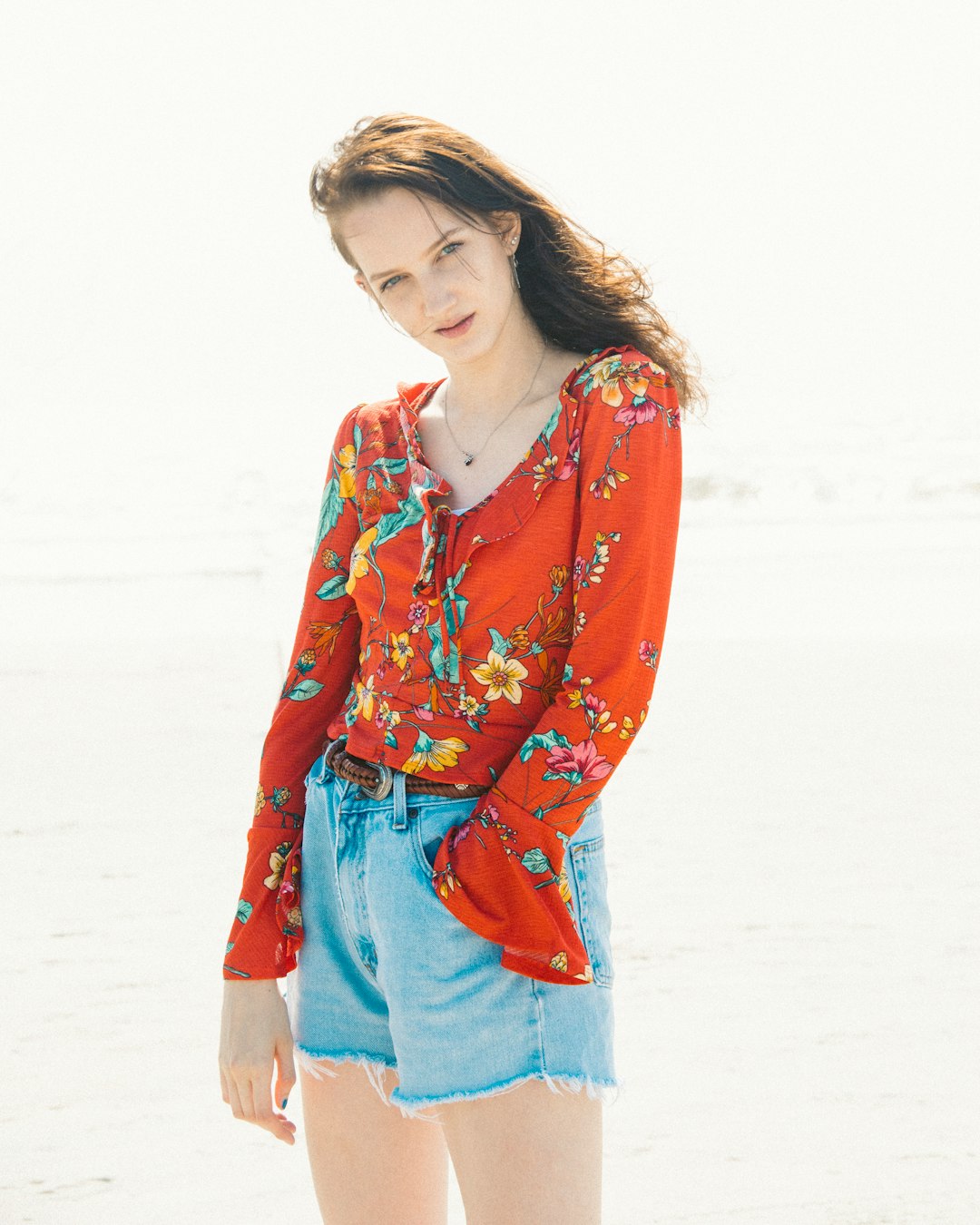 woman in red and blue floral long sleeve shirt standing on white sand during daytime