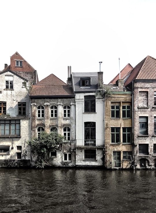 brown and white concrete building beside river during daytime in Ghent Belgium