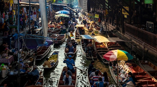 people riding on boat on river during daytime in Damnoen Floating Market Thailand