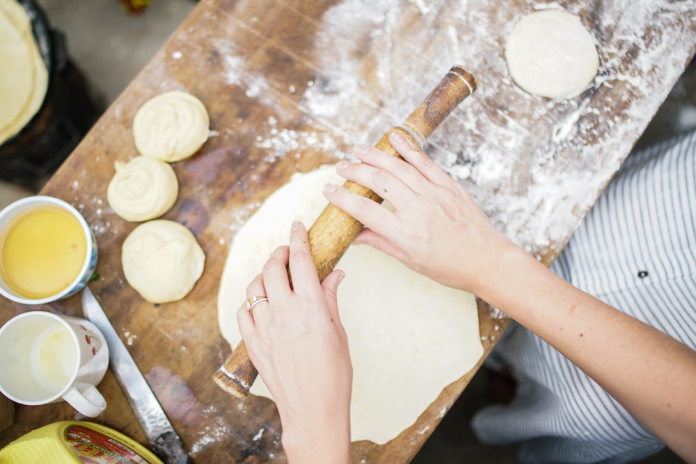 person holding brown wooden rolling pin