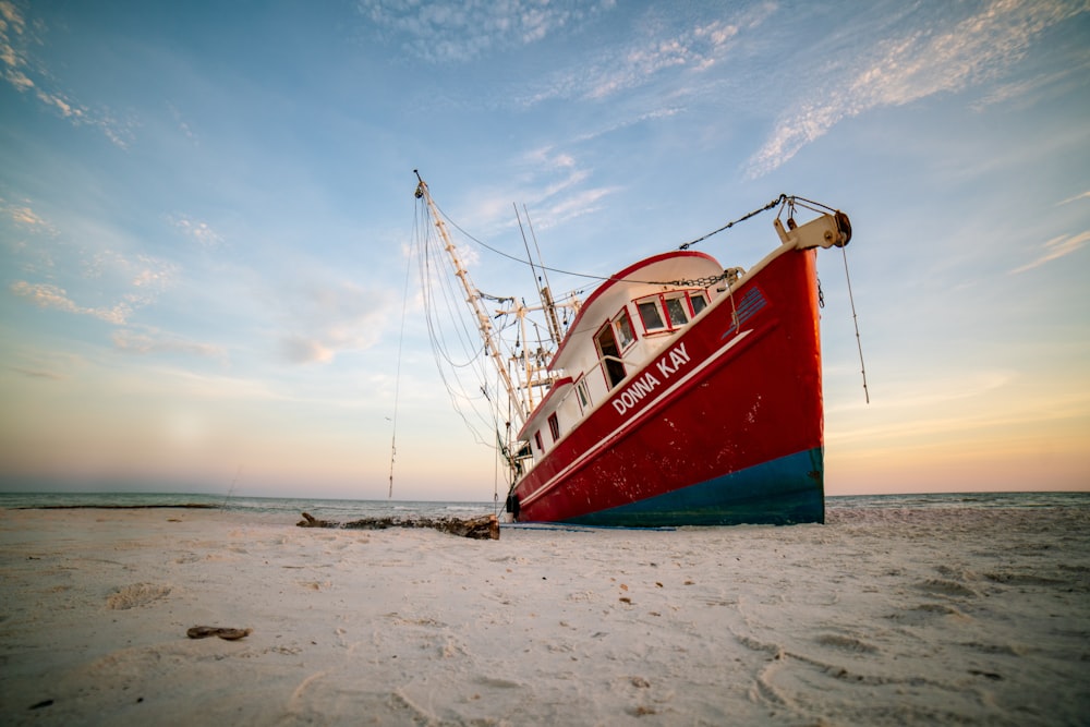 a red and blue boat sitting on top of a sandy beach