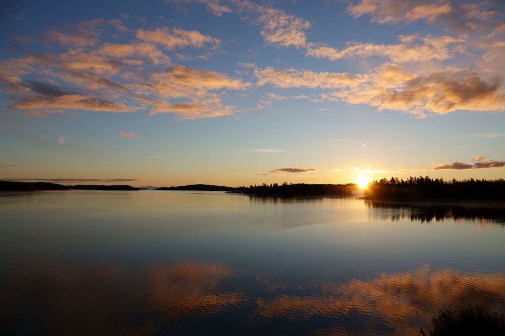 body of water near trees during sunset