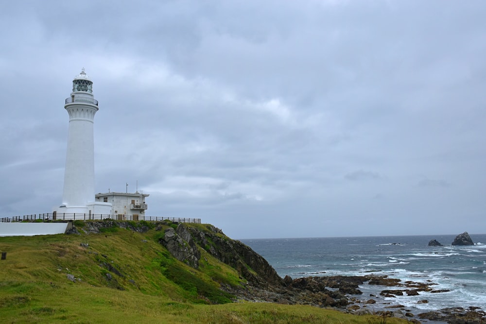 white lighthouse on green grass field near body of water during daytime