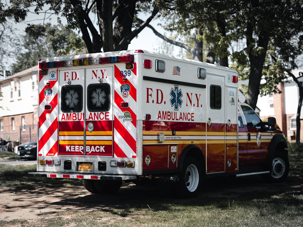 red and white ambulance truck parked near green trees during daytime