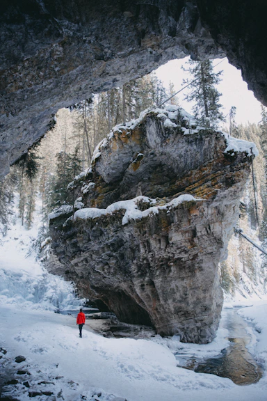 person in red jacket and black pants standing on snow covered ground near gray rocky mountain