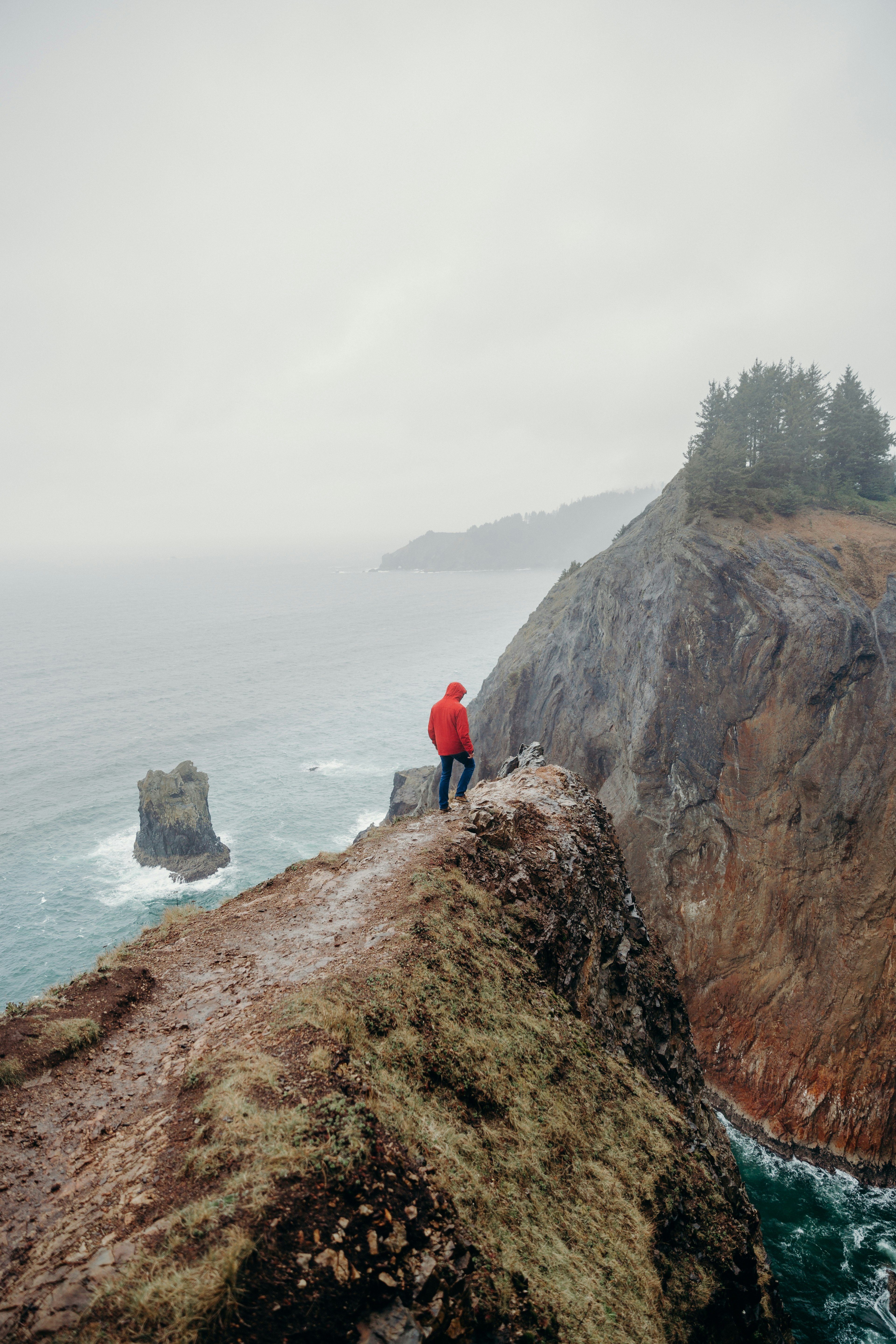 person in red jacket standing on brown rock formation near body of water during daytime