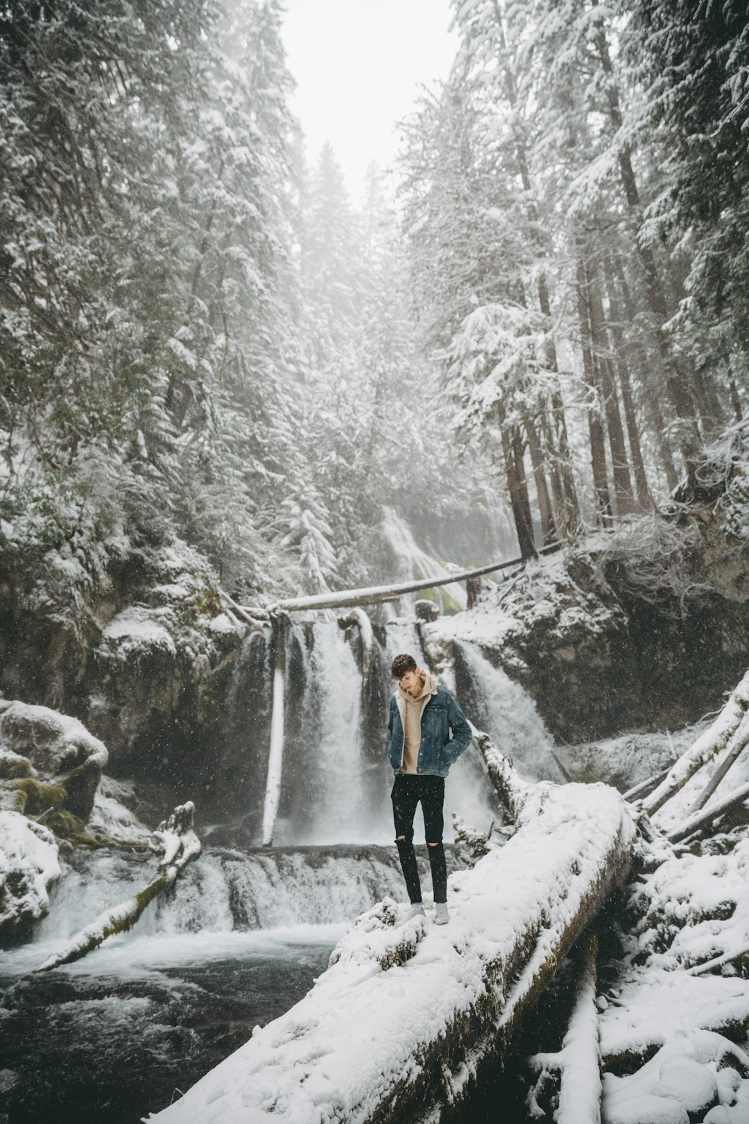 woman in black jacket and blue denim jeans standing on snow covered bridge