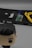 A book titled 'hackLOG' is prominently placed, accompanied by a small circuit board on top and a yellow Ethernet cable coiled beside it. In the foreground, a blurred figure of a small toy or figurine with dark hair is partially visible.