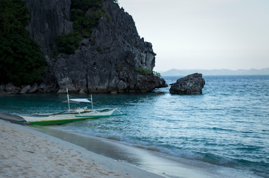 white and green boat on sea near rock formation during daytime in Coron Philippines