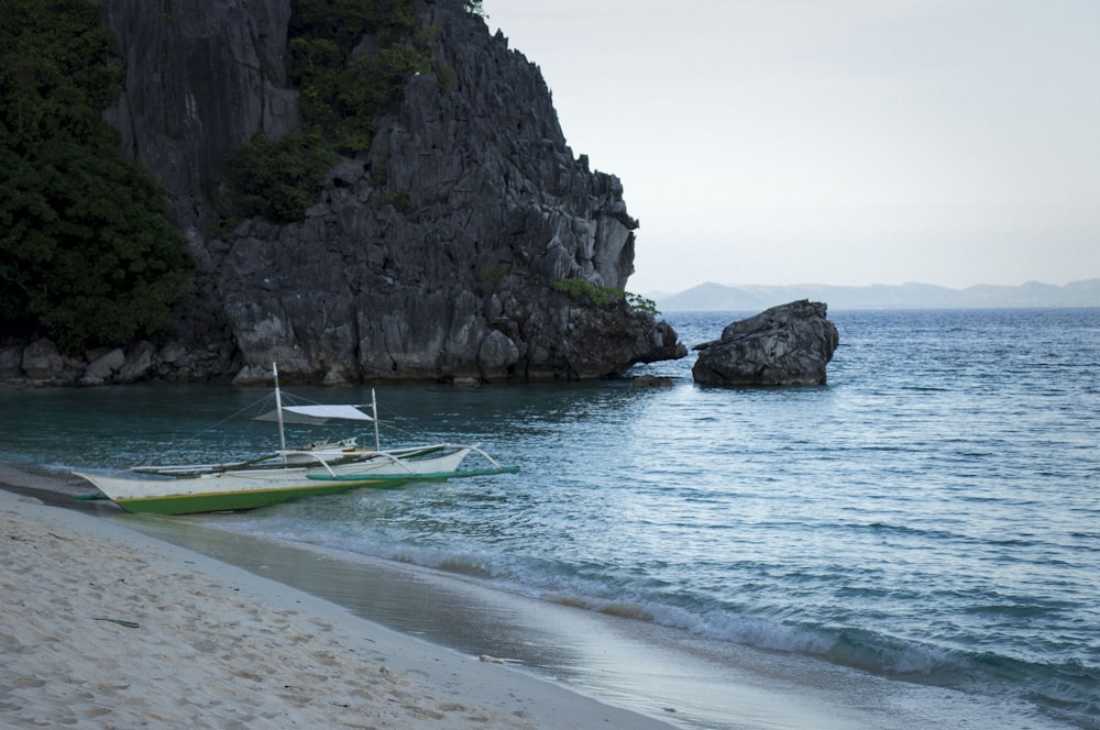 white and green boat on sea near rock formation during daytime