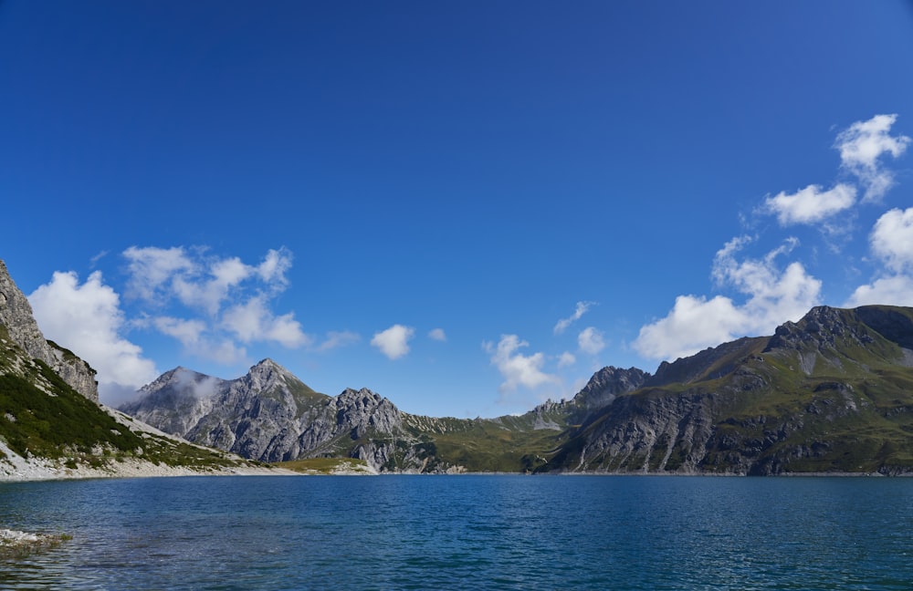 green and white mountain beside body of water under blue sky during daytime