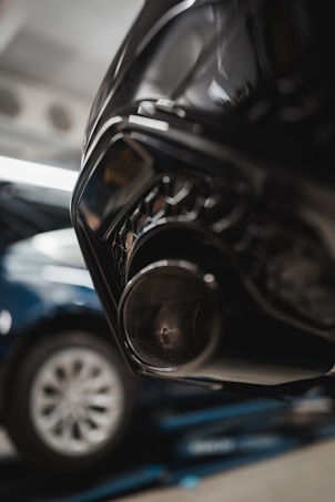 Close-up of a car's exhaust pipe with a blurred vehicle in the background, highlighting automotive components.