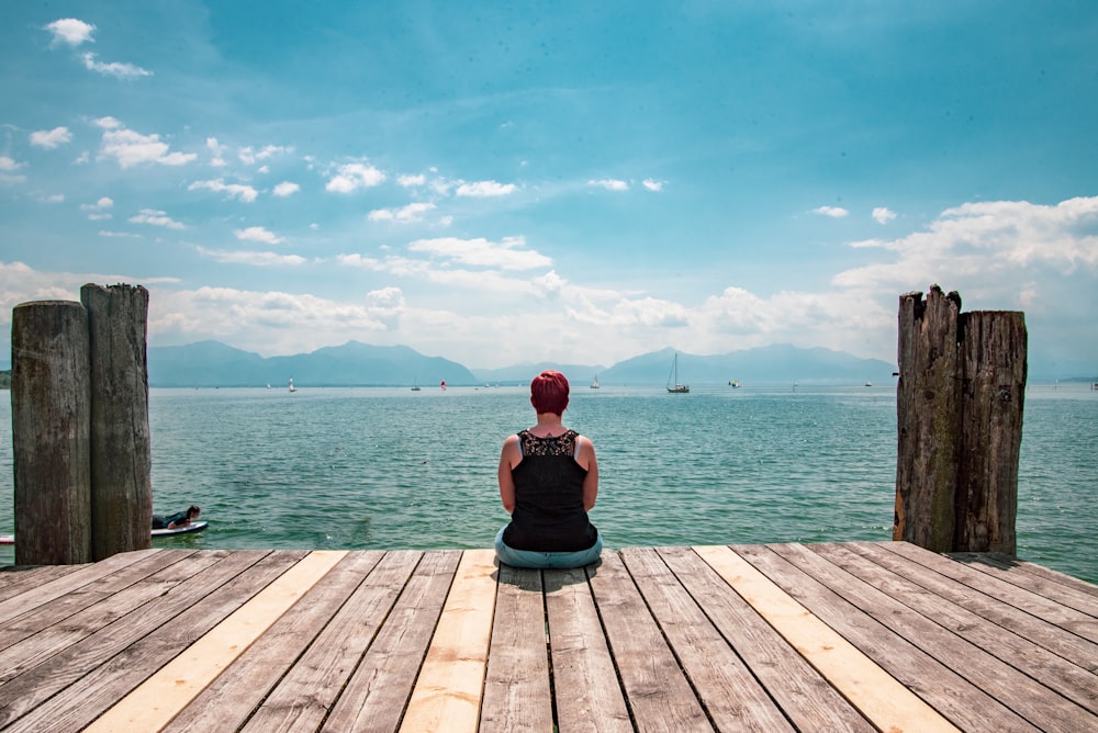 man in red t-shirt sitting on wooden dock during daytime