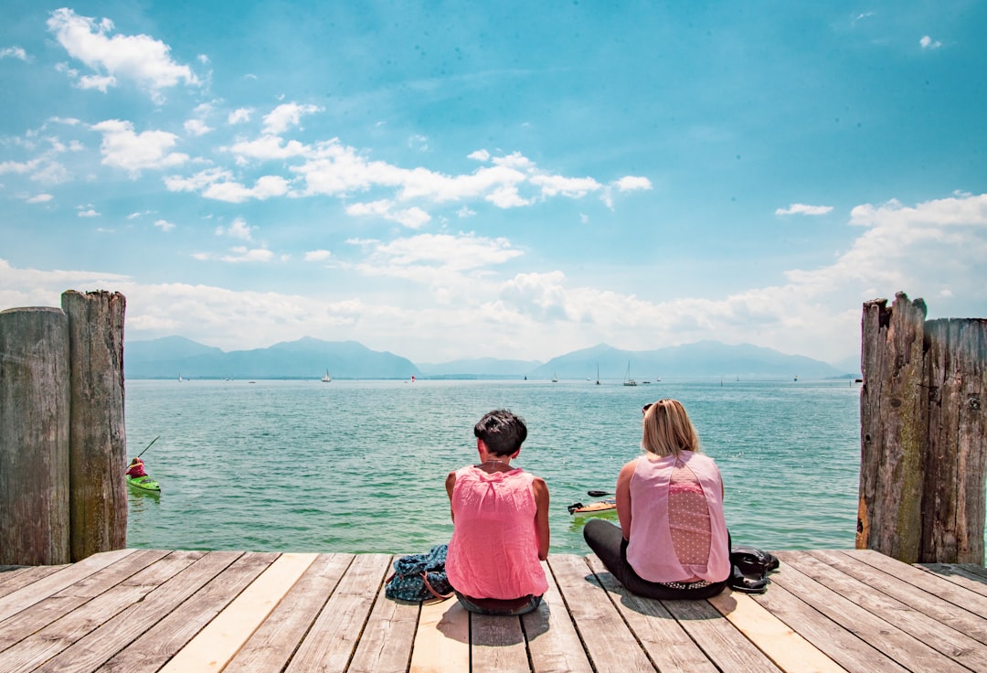 woman in pink hoodie sitting on brown wooden dock during daytime