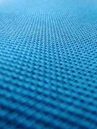 A close-up view of a textured surface with a repeating pattern, likely a fabric or material with a woven or mesh-like structure. The texture appears to be uniform and consists of small, evenly distributed bumps or nodes.