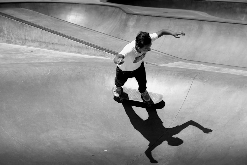 grayscale photo of man in white t-shirt and black pants doing skateboard stunts