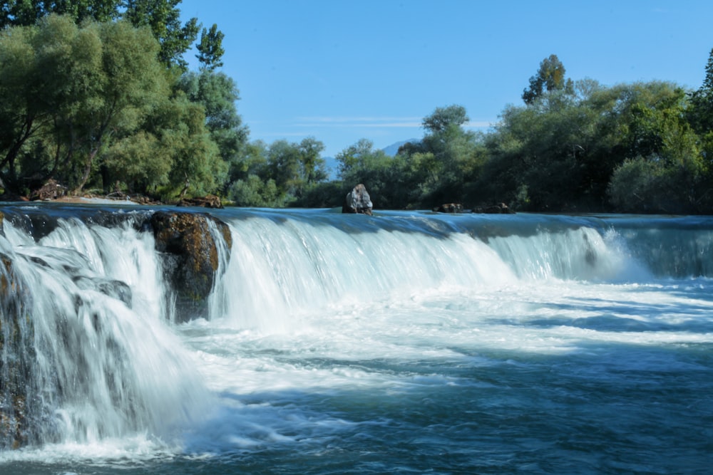 Cascadas cerca de árboles verdes bajo el cielo azul durante el día