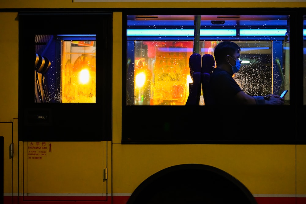 Homme en veste noire assis à l’intérieur d’un bus jaune pendant la journée