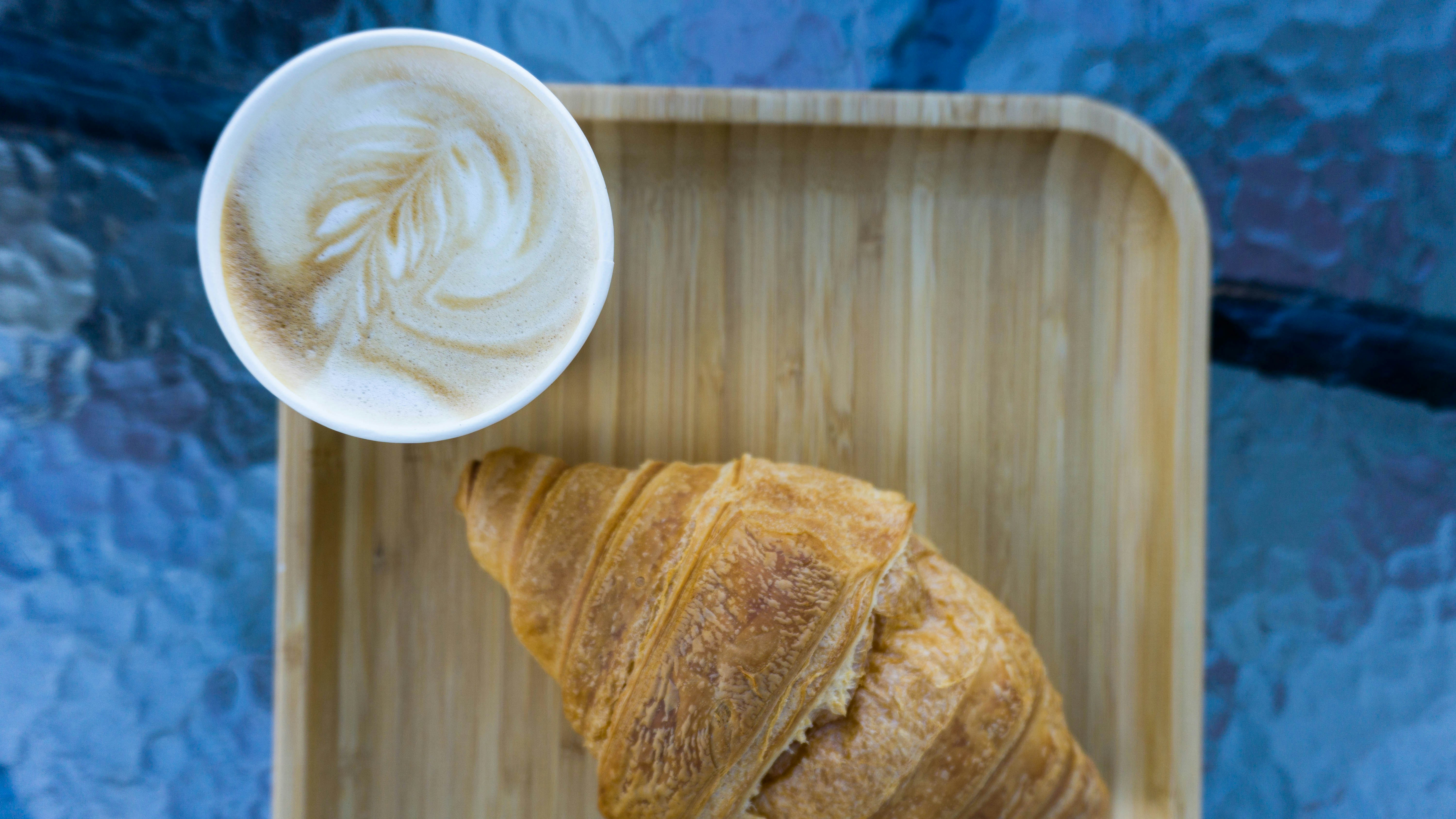 Croissant on a bamboo tray beside a latte