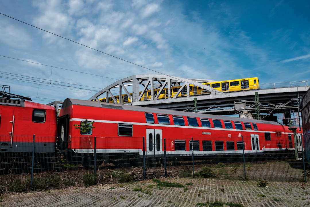 red and white train on rail tracks under blue sky and white clouds during daytime