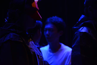 Theater workshop scene with expressive faces and dynamic gestures under deep blue lighting.