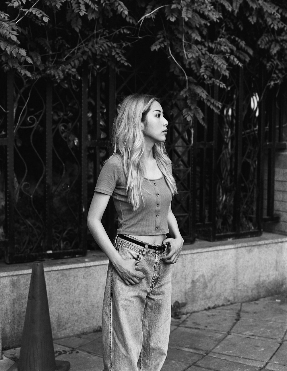 woman in tank top and denim jeans standing on concrete pavement in grayscale photography