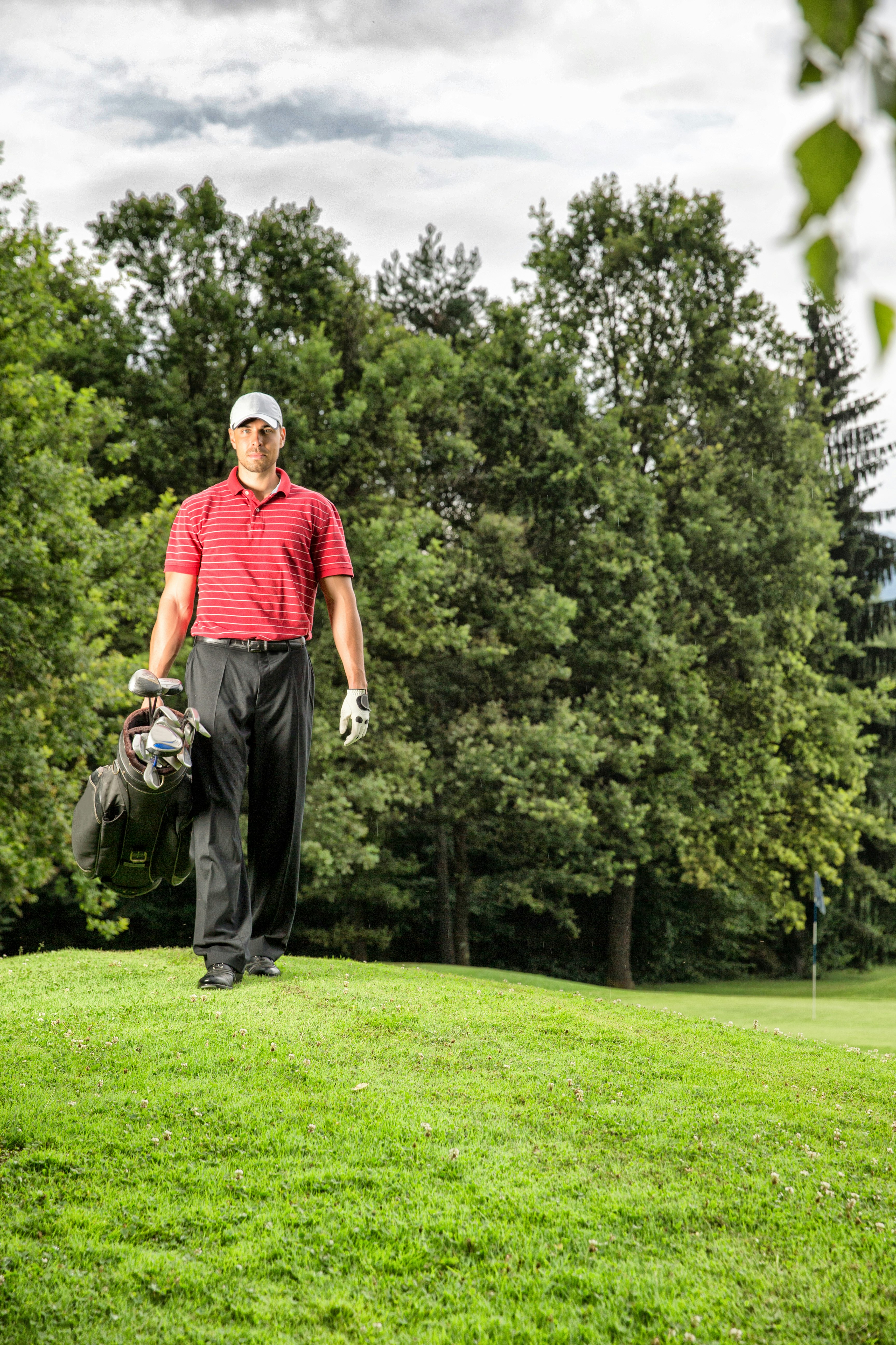 man in red polo shirt and black pants walking on green grass field during daytime