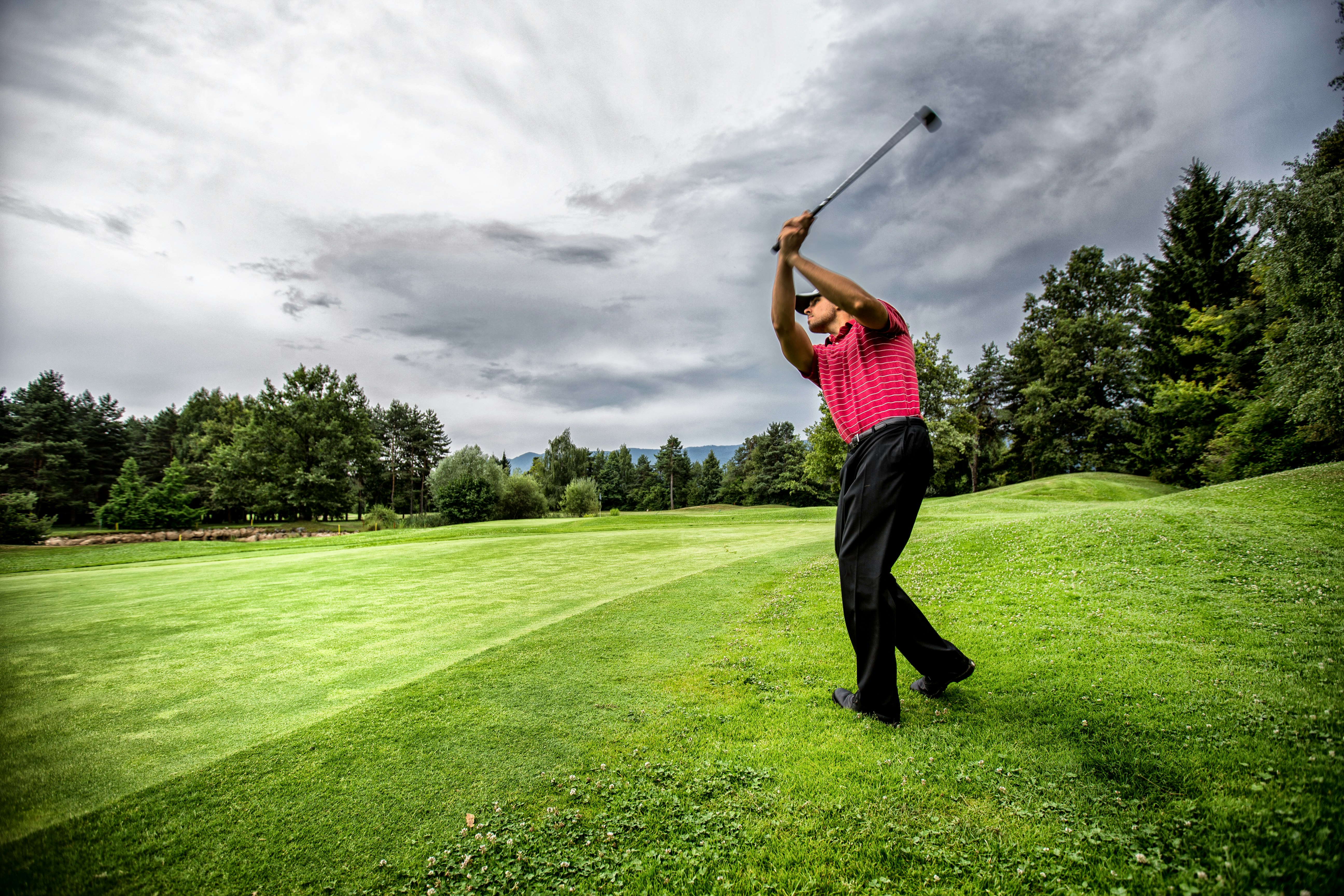 man in red t-shirt and black pants playing golf during daytime