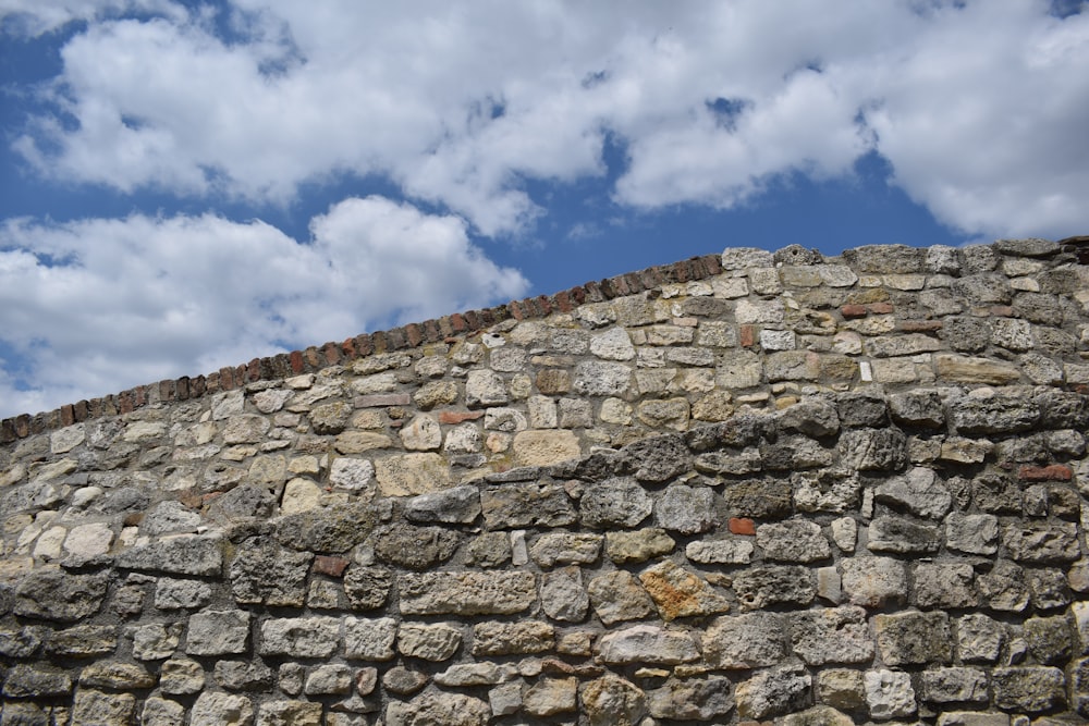 pared de ladrillo gris bajo el cielo azul y nubes blancas durante el día