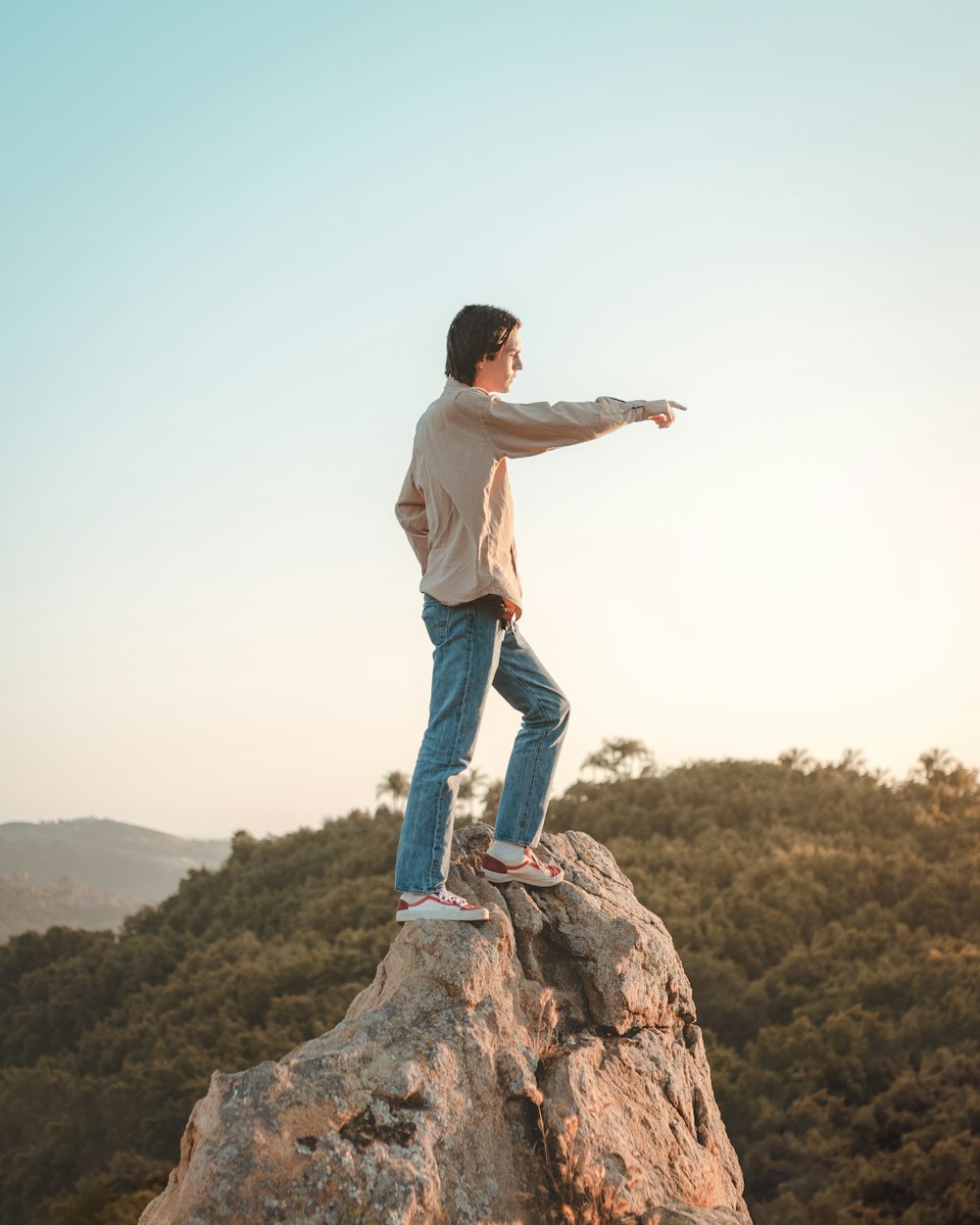 man in white t-shirt and blue denim jeans standing on brown rock during daytime