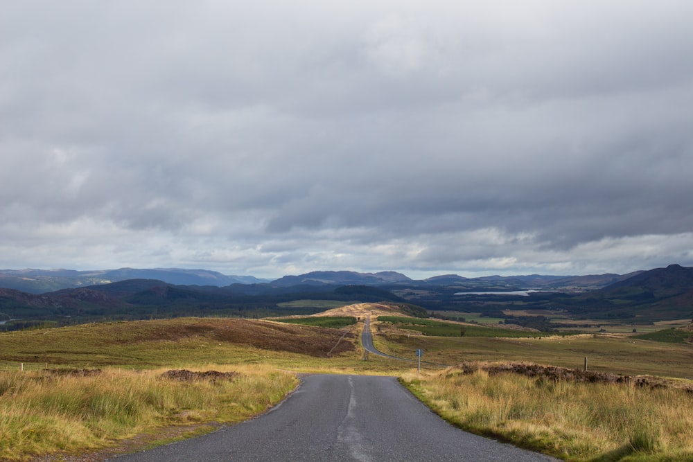 black asphalt road between green grass field under white cloudy sky during daytime